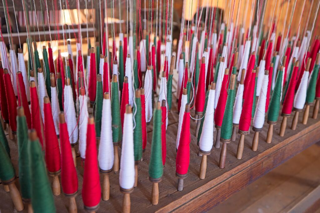 Dozens of spindles of white, green, and red thread arrayed on a wooden platform.