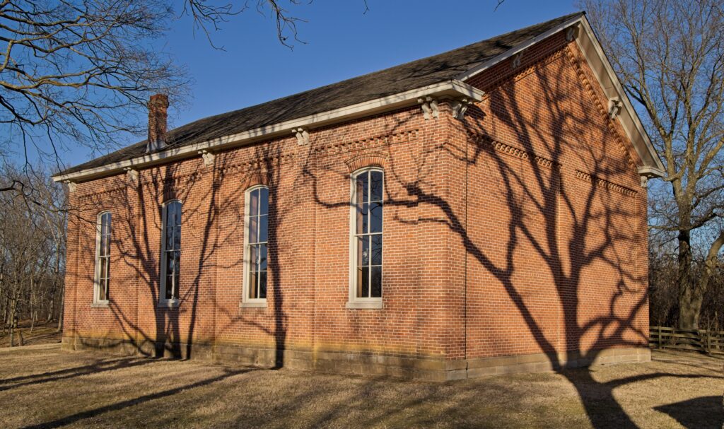 A brick building with the shadow of a tree on the side in late afternoon.