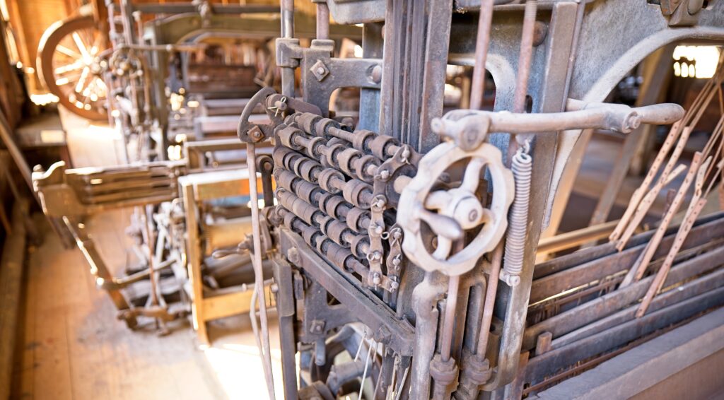 An Industrial Revolution era loom seen from the side with several metal wheels arrayed in a rectangular pattern.